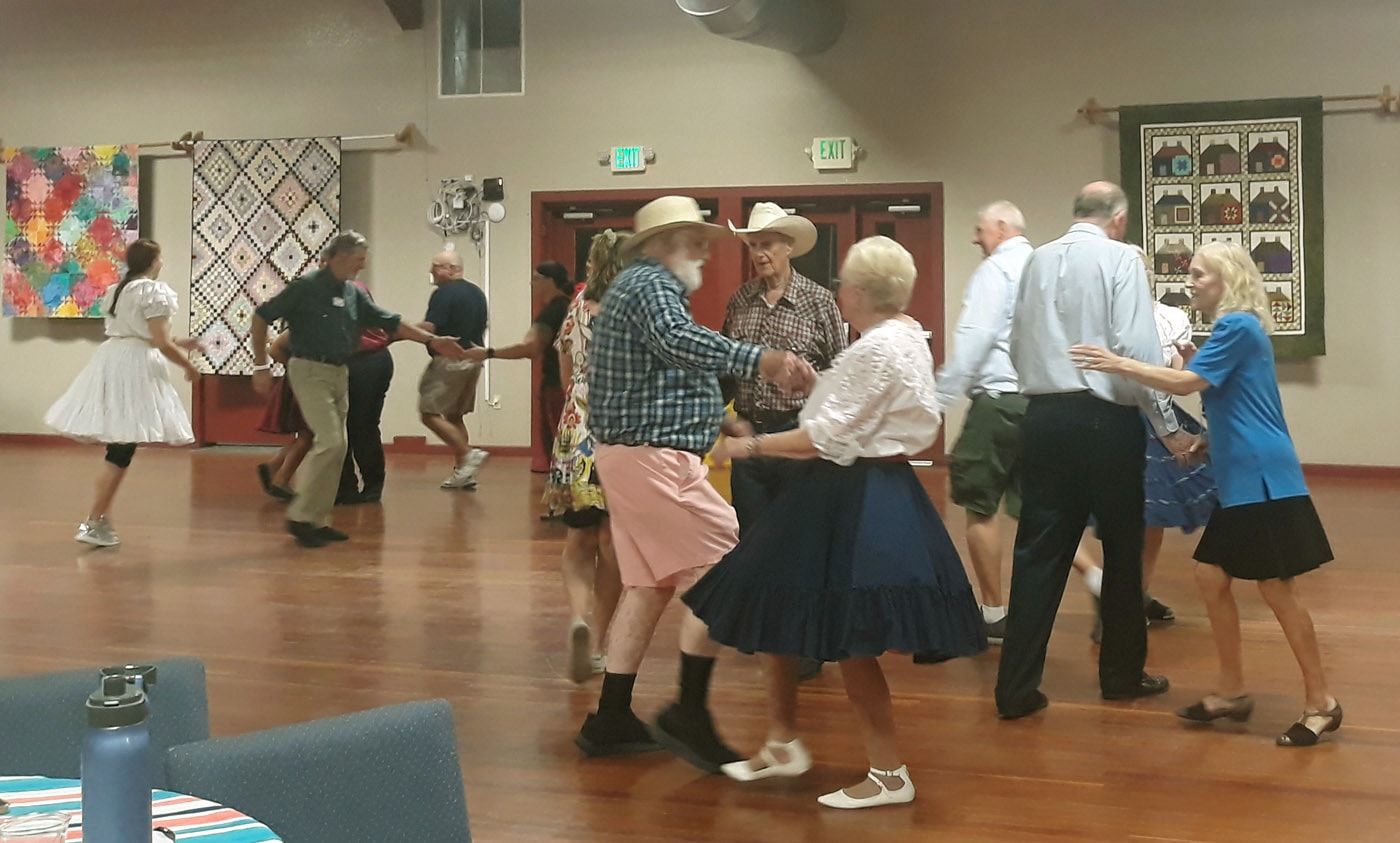 Square dance caller leading couples in traditional western attire with quilts on the walls in Northern California