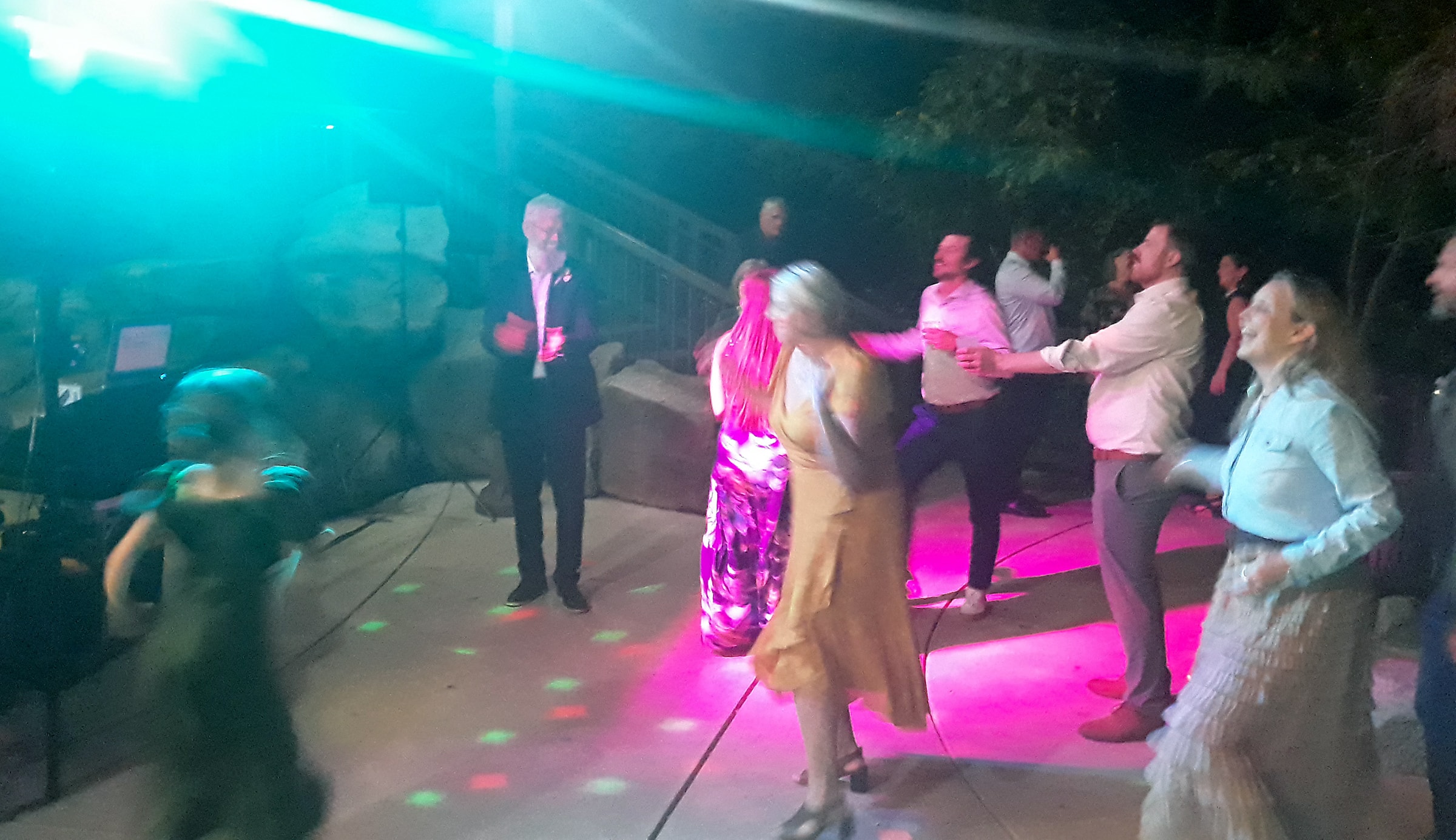 Wedding guests dancing under vivid pink and teal DJ lighting at an outdoor reception in Grants Pass, Oregon